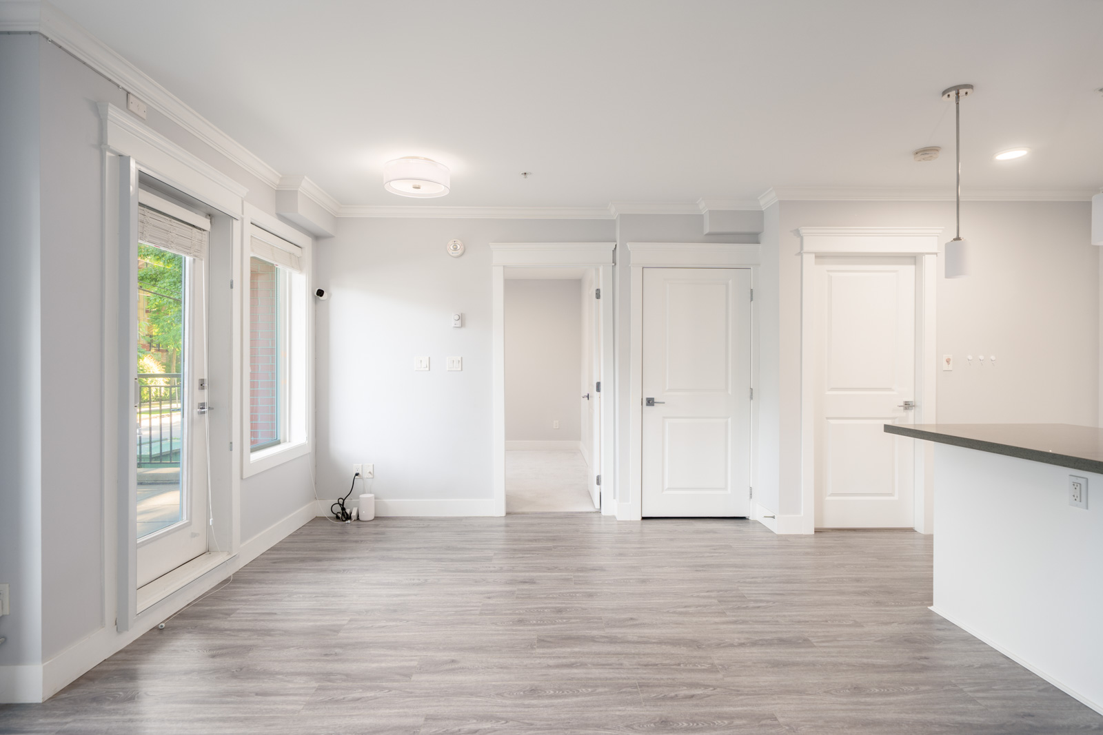 Unfurnished modern apartment interior with light gray walls, wood floors, white doors, and large windowed patio door allowing natural light inside.