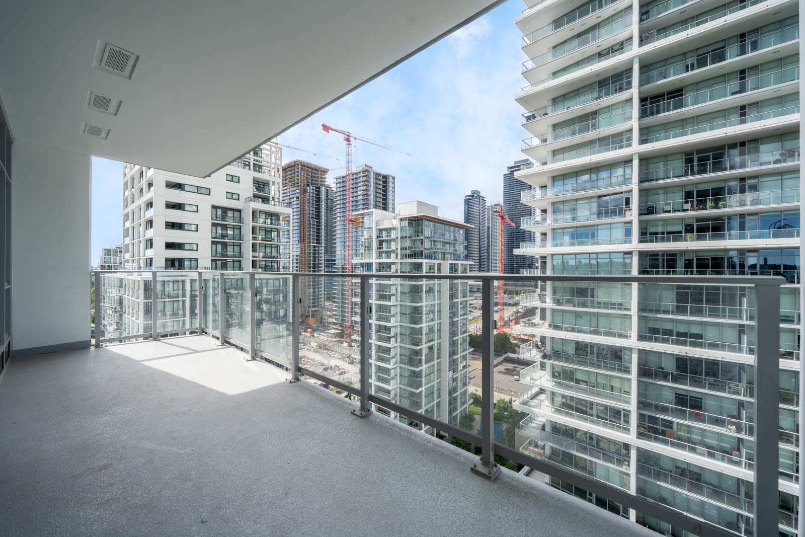 View from a modern balcony overlooking nearby high-rise buildings and a construction site with cranes in an urban area.