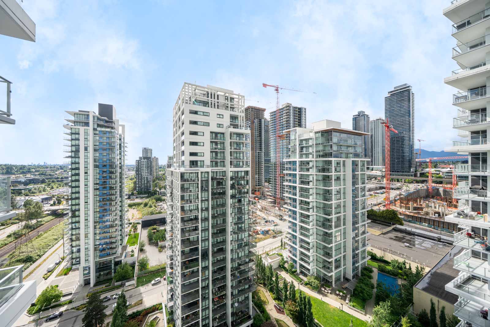 High-rise residential buildings with glass balconies, construction cranes, and skyscrapers in the background under a clear sky.