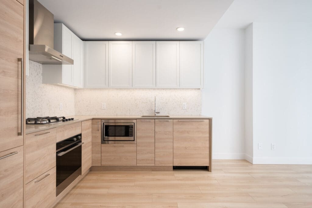 Modern kitchen with light wood cabinets, white upper cabinets, stainless steel appliances, gas stove, built-in oven, microwave, and light-colored flooring.