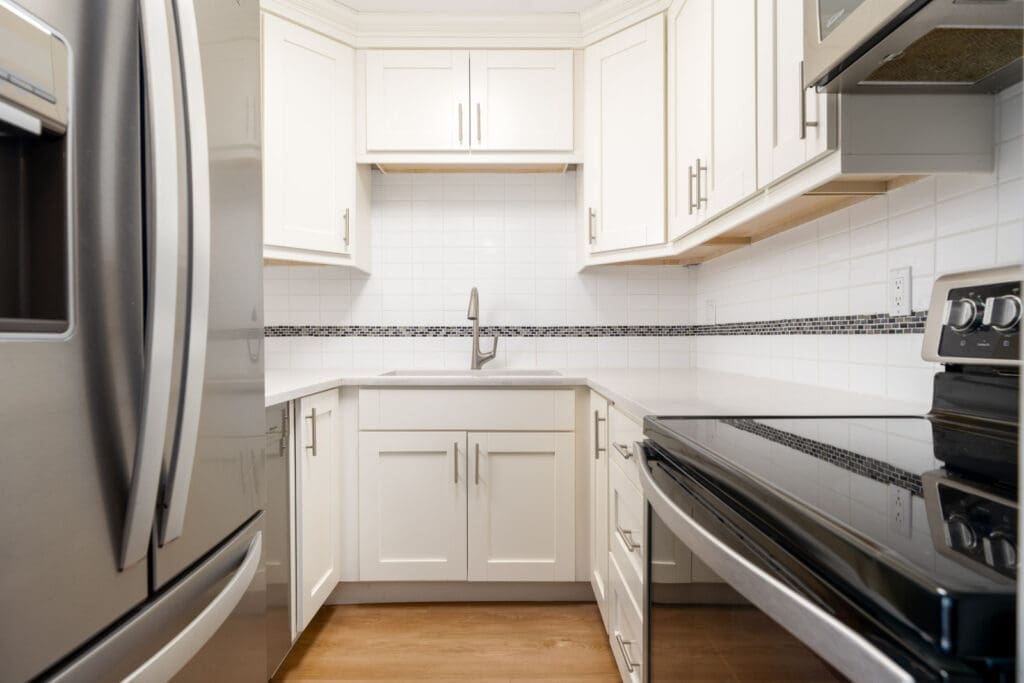 Modern kitchen with white cabinets, stainless steel appliances, a tile backsplash, and a single-handle faucet over a corner sink.