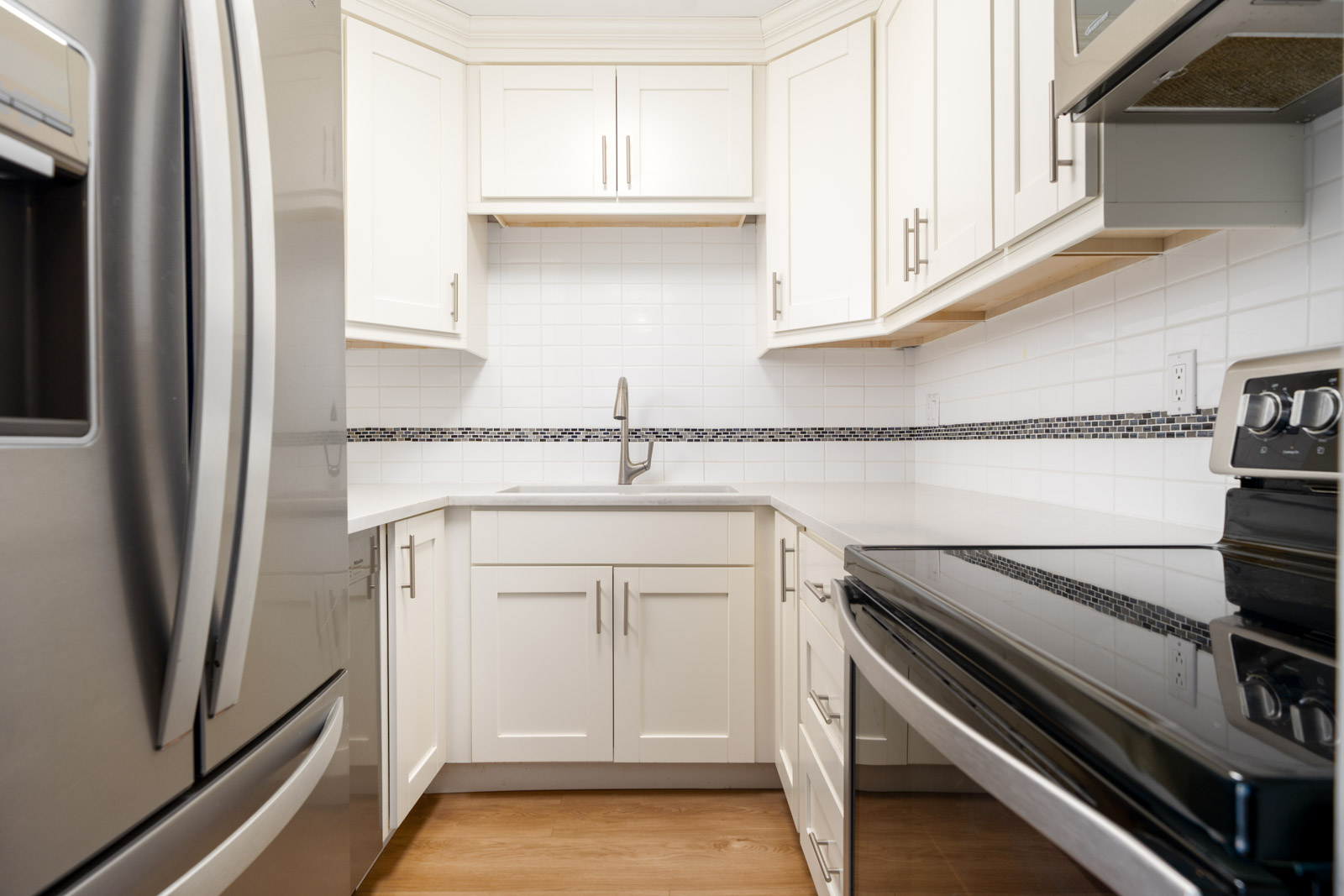 Modern kitchen with white cabinets, stainless steel appliances, a tile backsplash, and a single-handle faucet over a corner sink.
