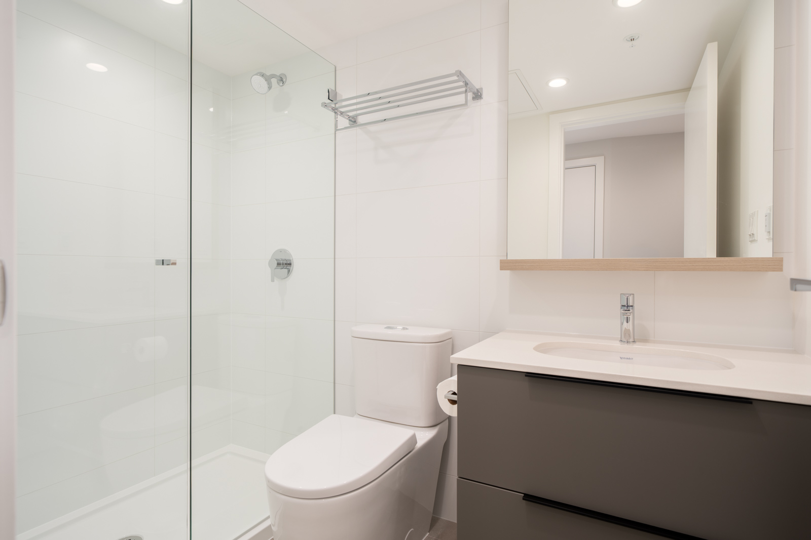 Modern bathroom with a glass-enclosed shower, white toilet, wall-mounted towel rack, and a vanity with sink and large mirror.