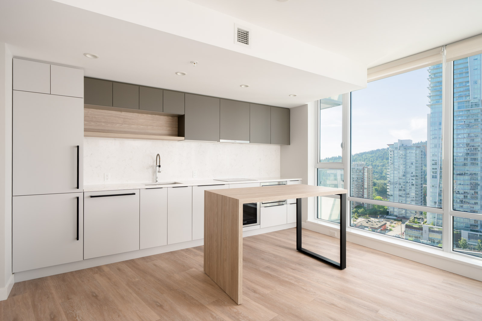 Modern, minimalist kitchen with white and grey cabinets, a built-in oven, a light wood floor, and a large window offering a city view.