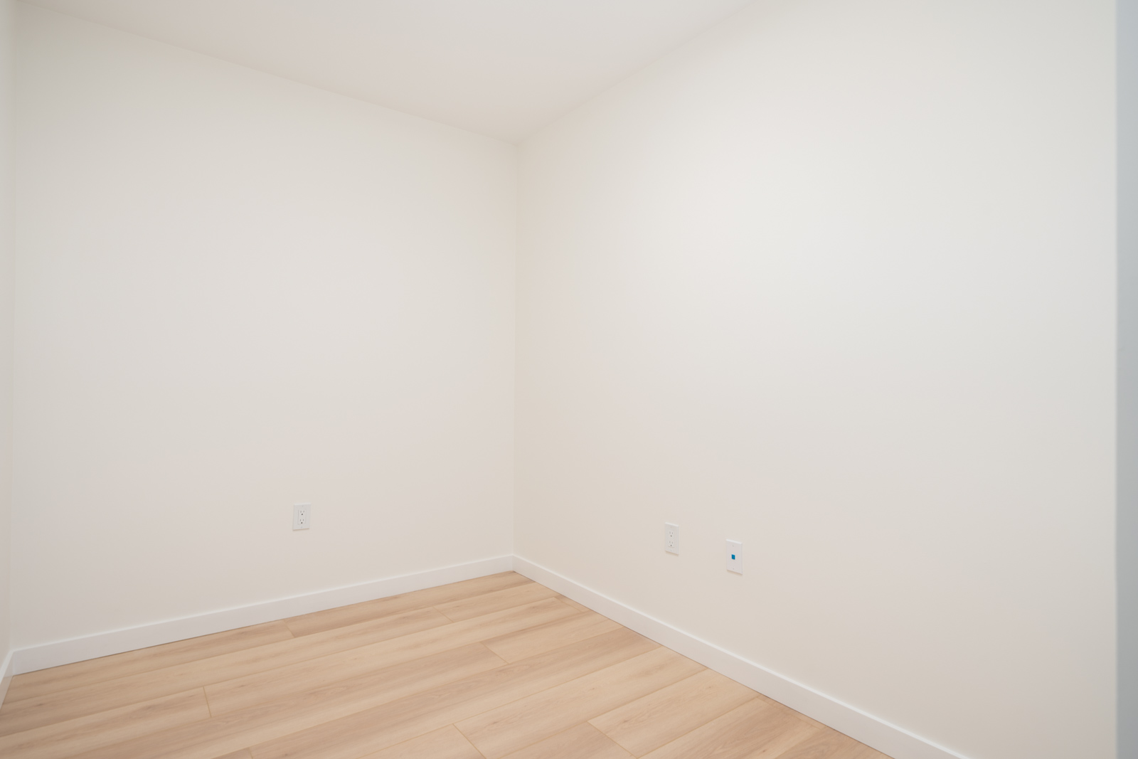 Empty room with white walls, light wood flooring, two electrical outlets, and no furniture or decorations.