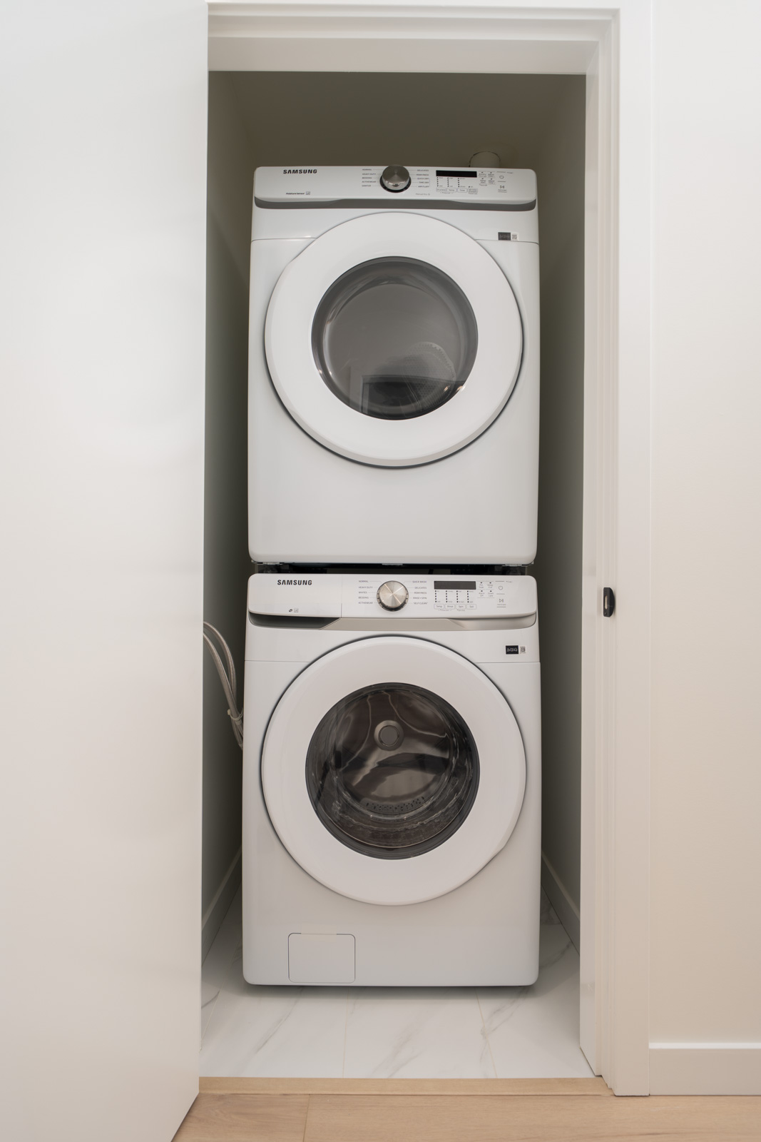 A stacked front-loading washer and dryer set installed in a small white closet with the door partially open.