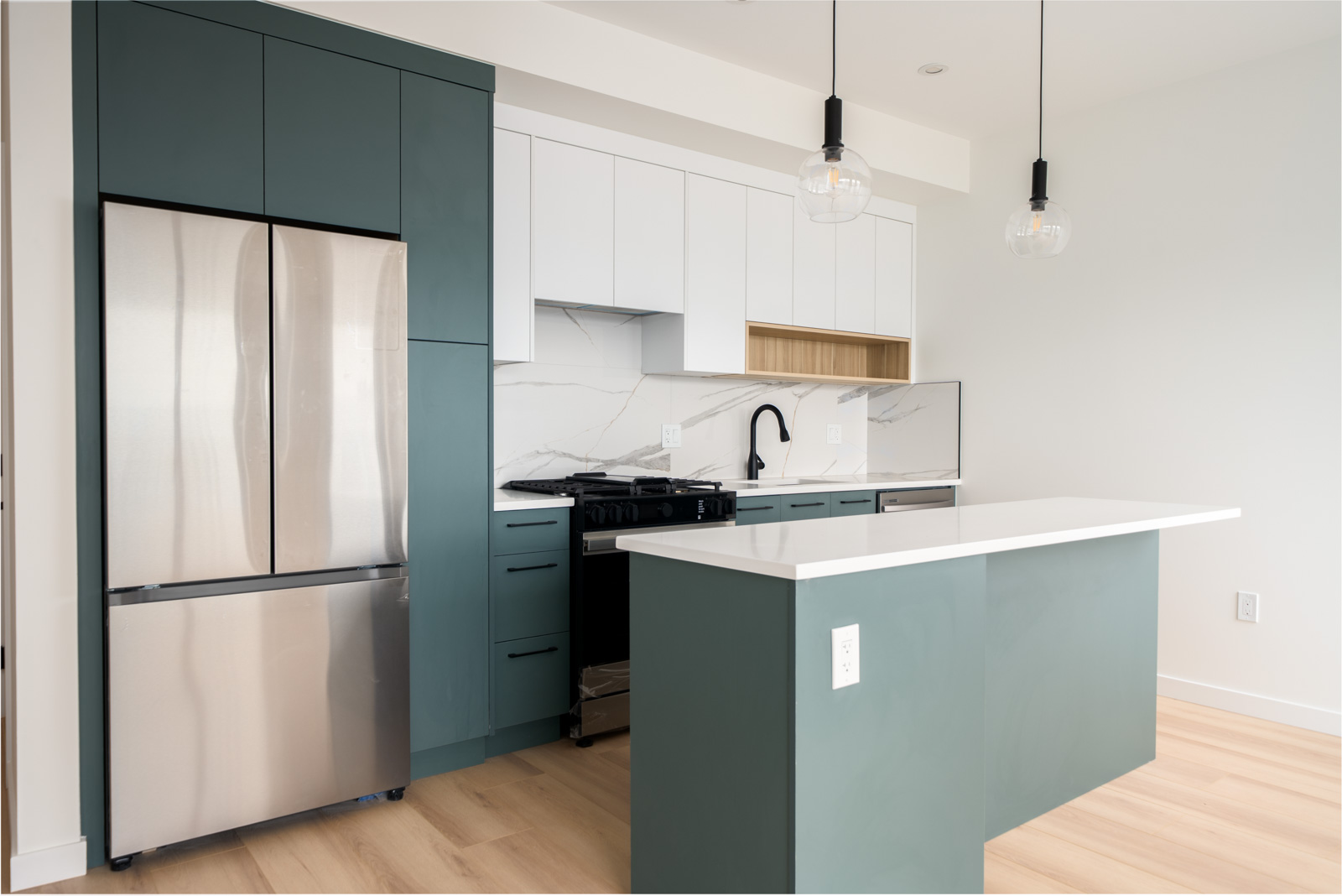 Modern kitchen with green and white cabinets, stainless steel appliances, marble backsplash, island with white countertop, and two pendant lights.
