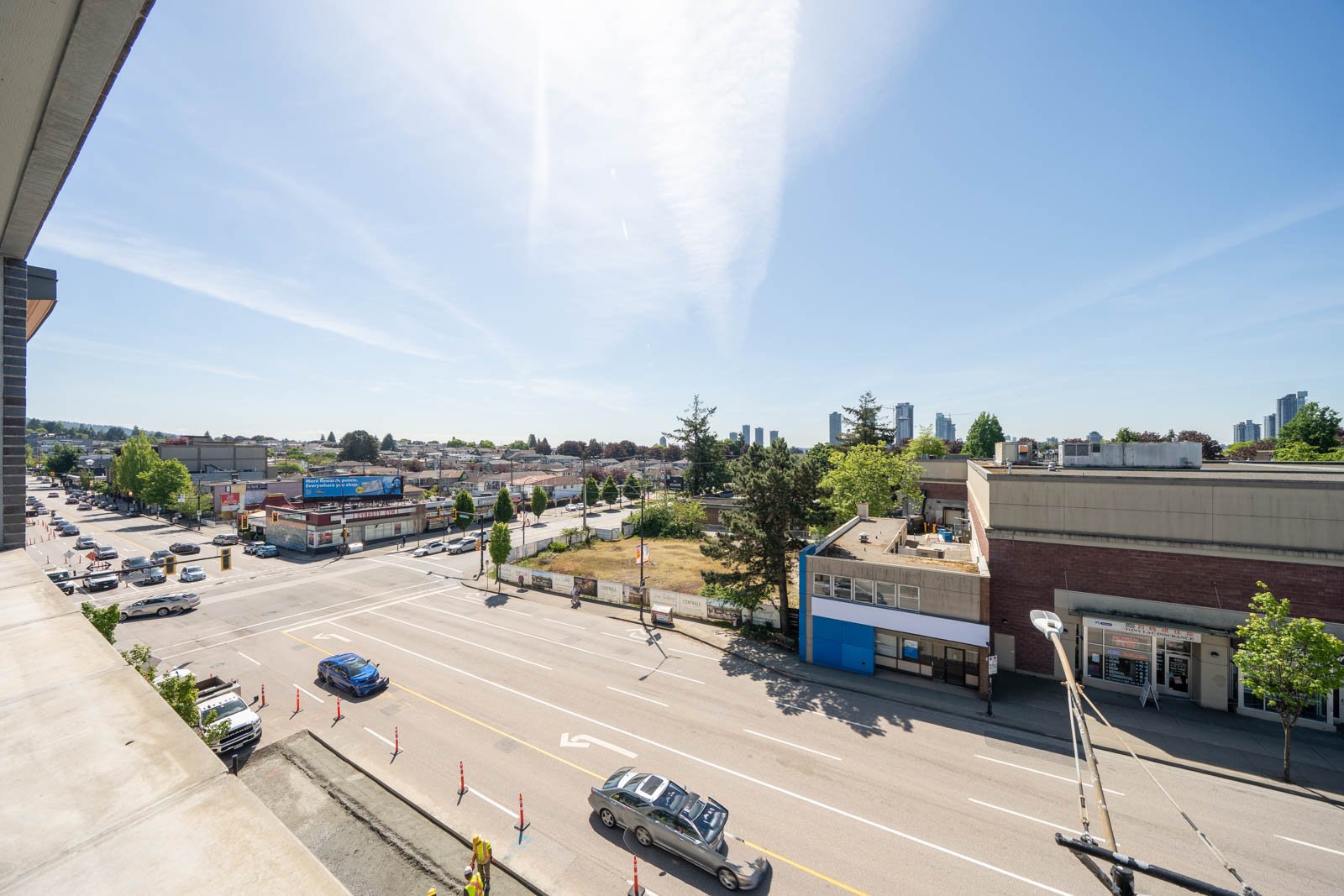 A wide view of a busy intersection with cars, buildings, trees, and clear blue sky on a sunny day.