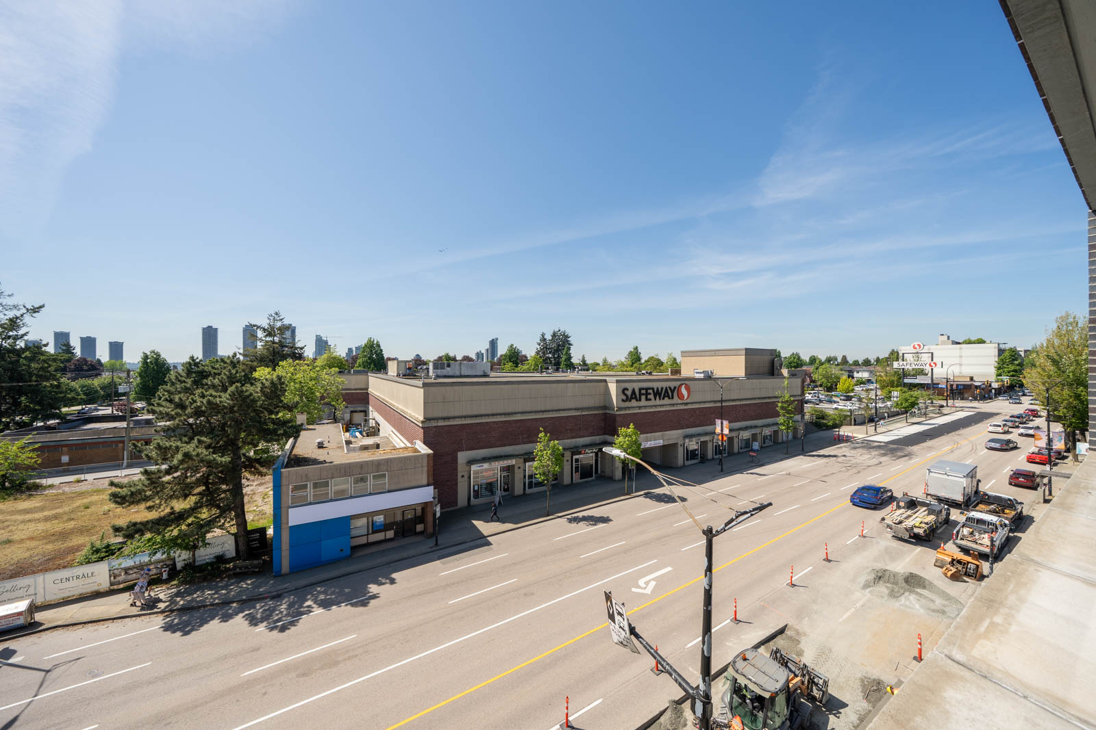 A wide street view featuring a Safeway grocery store, some parked cars, traffic cones, and nearby buildings on a clear, sunny day.