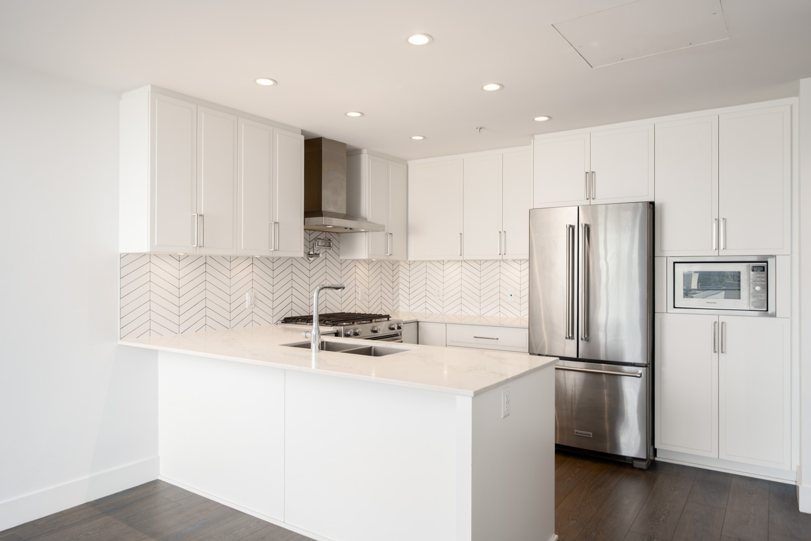 Modern kitchen with white cabinets, stainless steel appliances, herringbone tile backsplash, and a marble countertop island with a built-in sink.