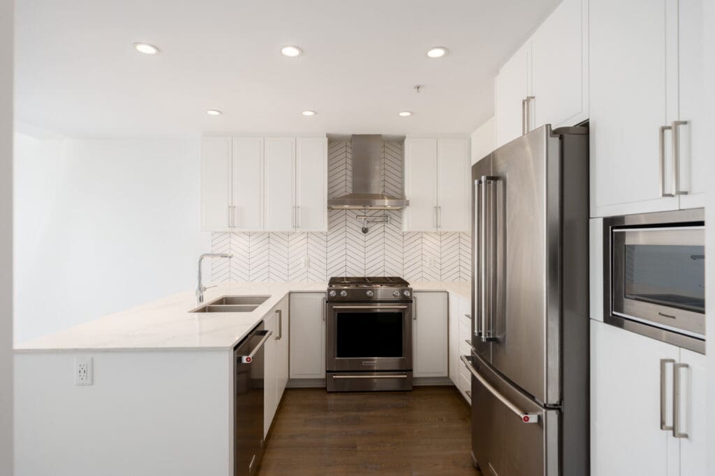 Modern kitchen with white cabinets, stainless steel appliances, a herringbone tile backsplash, and a white marble countertop.