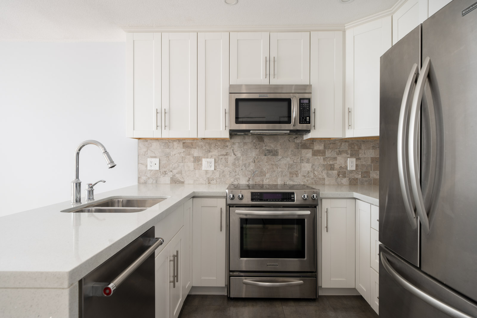 Modern kitchen with white cabinets, stainless steel appliances, built-in microwave, electric stove, sink, and stone tile backsplash.