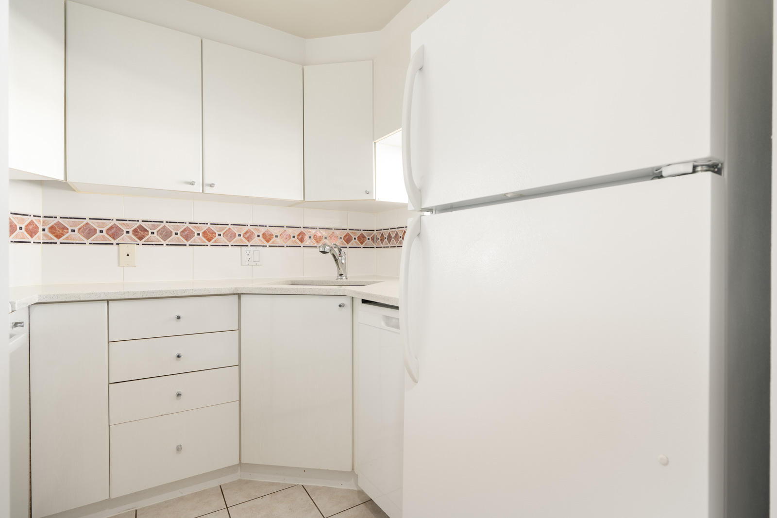 White kitchen with upper and lower cabinets, a large refrigerator, dishwasher, sink, and patterned tile backsplash above the counter.