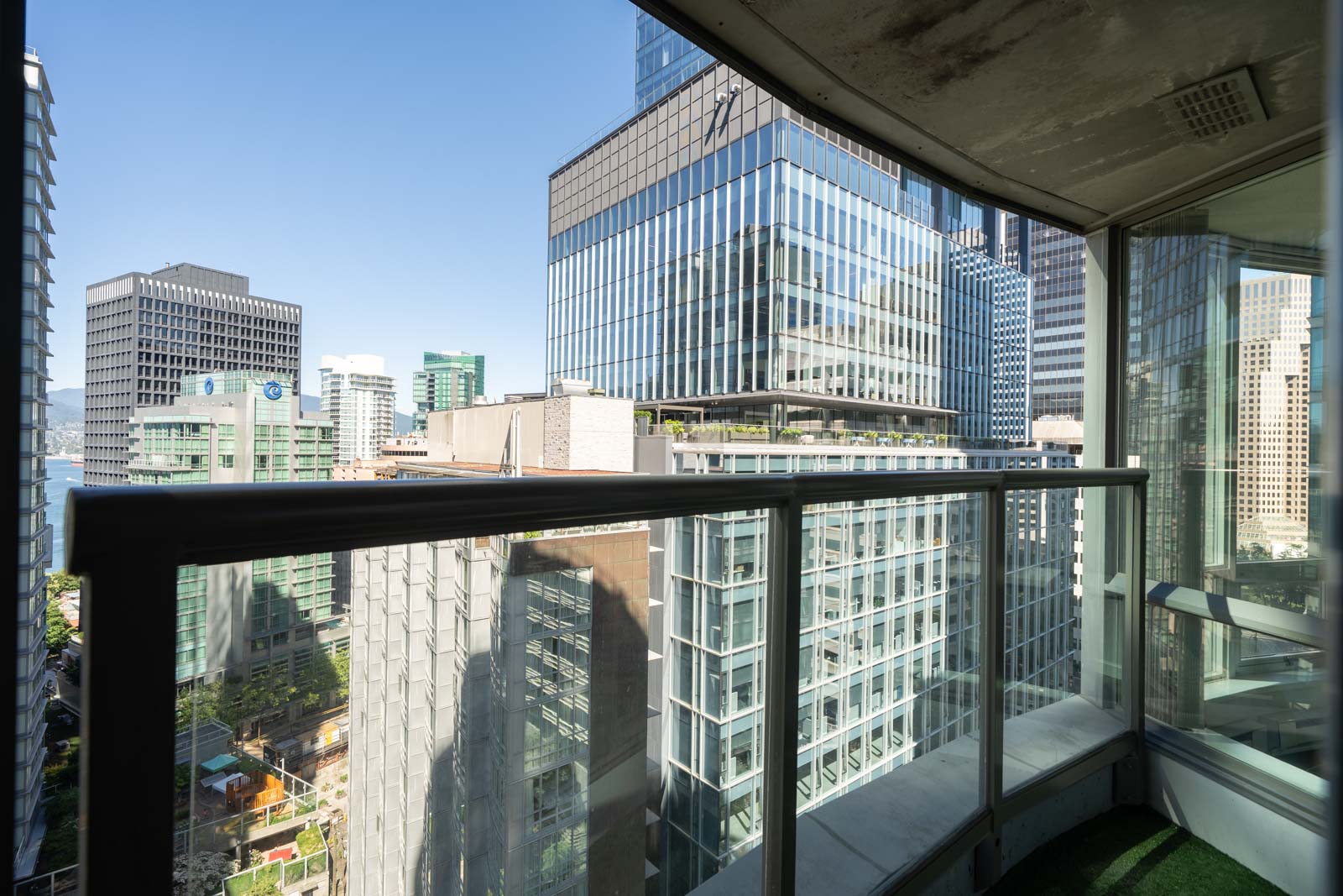 View from a balcony showing modern glass office buildings in a city center under a clear blue sky.