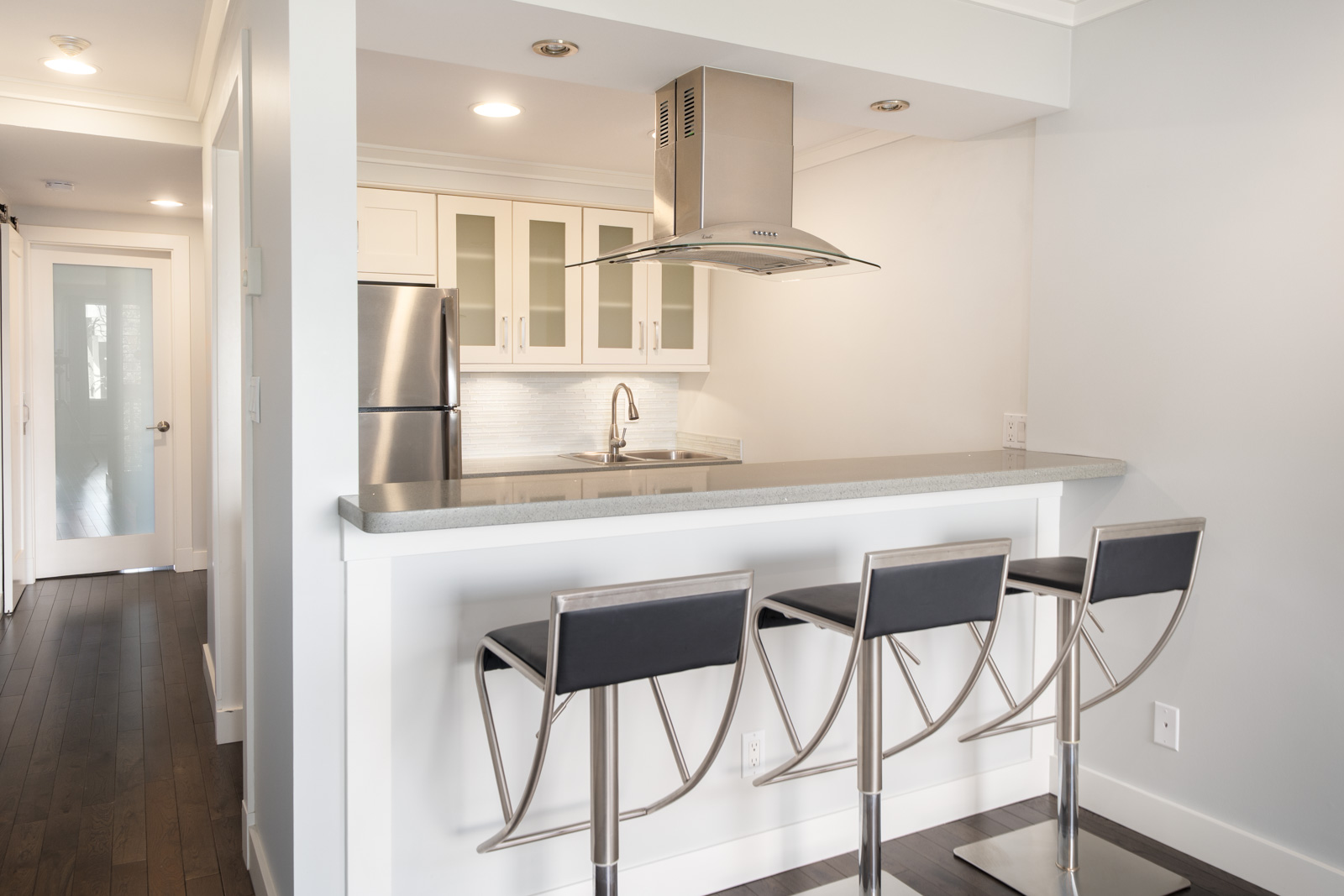 Modern kitchen with stainless steel appliances, white cabinets, an island with a gray countertop, and three metal barstools with black seats.