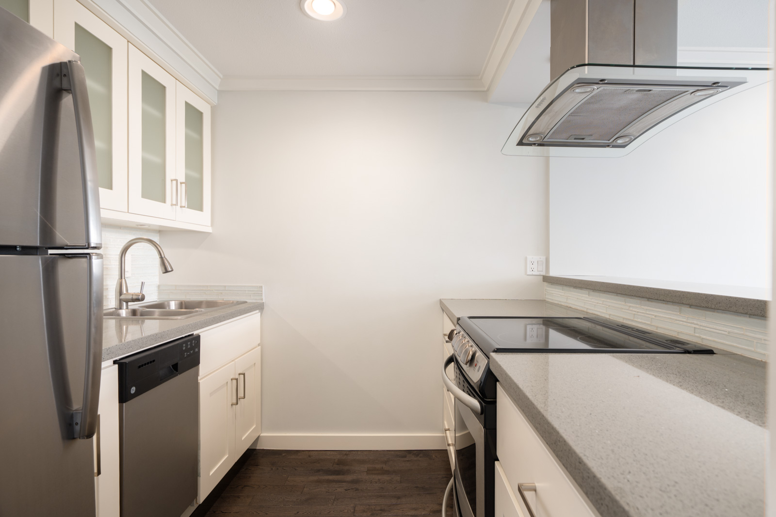 Modern galley kitchen with stainless steel appliances, white cabinets, gray countertops, and dark wood flooring.