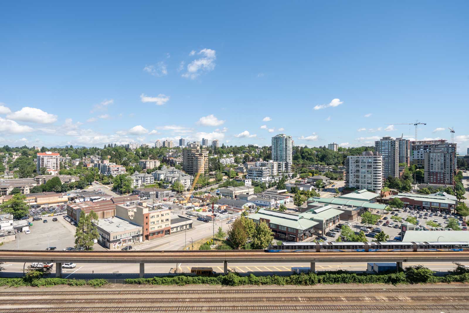 A cityscape view with mid-rise buildings, streets, parking lots, and a railway in the foreground under a clear blue sky.