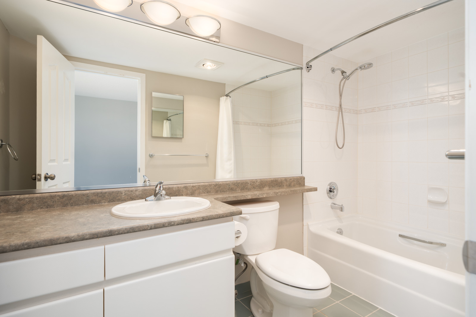 Modern bathroom with a large mirror, single sink, toilet, and white bathtub with a showerhead and a curved shower rod.