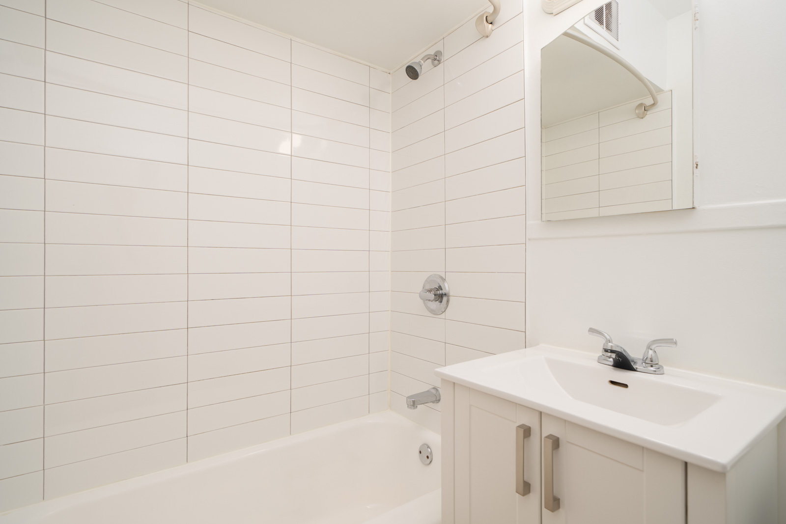White bathroom with a tiled shower-tub combo, a wall-mounted showerhead, and a white vanity with a sink and mirror above it.