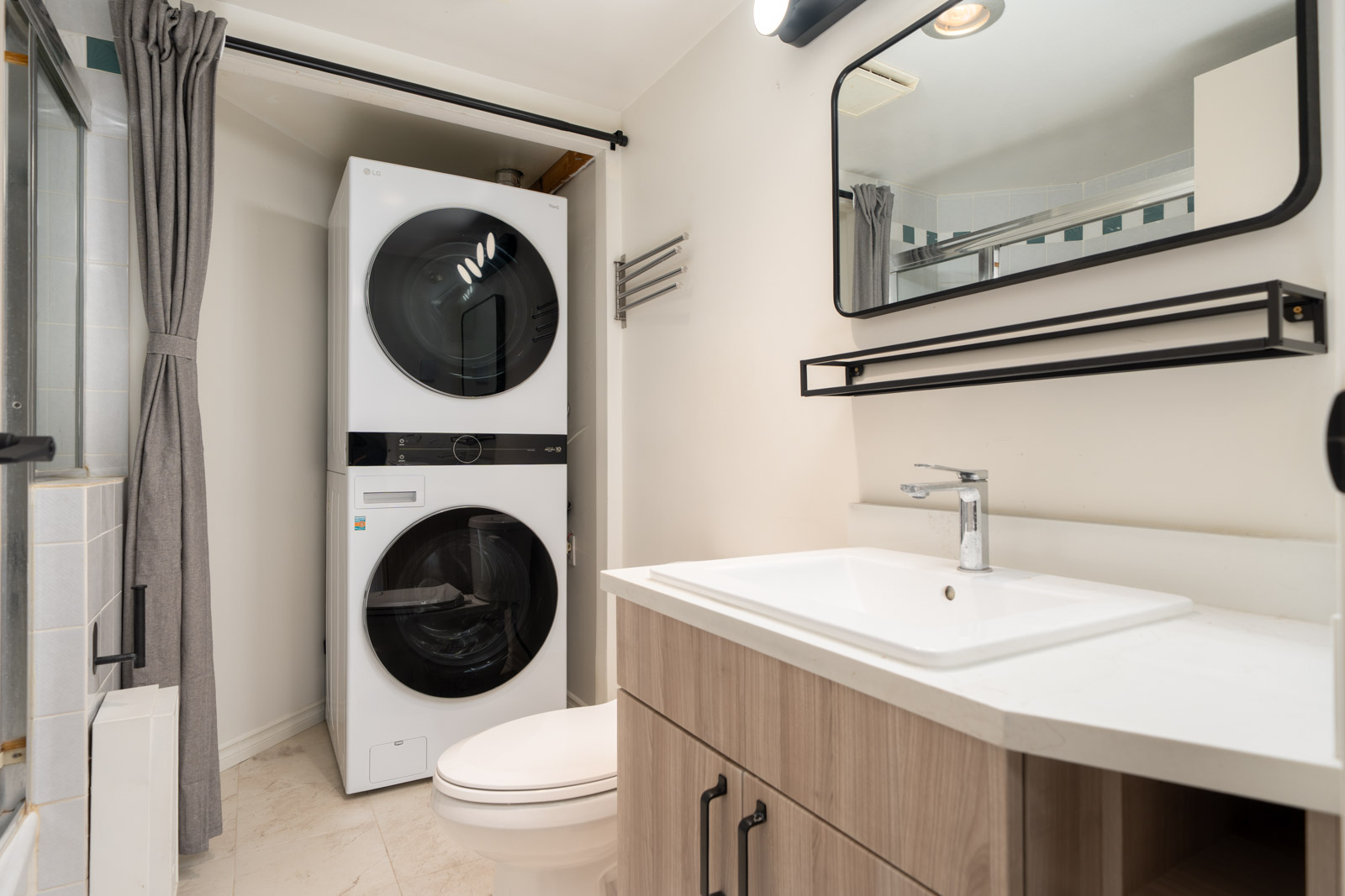 A modern bathroom with a sink, mirror, wooden vanity, and a stacked washer and dryer next to a toilet.