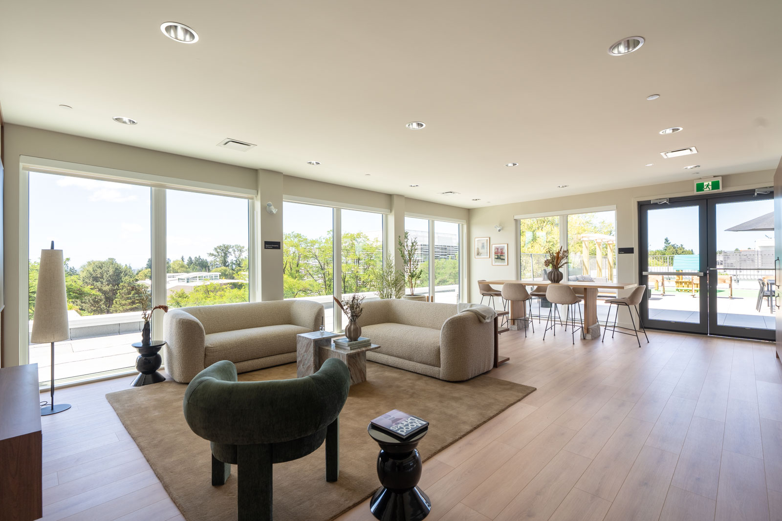 A modern living and dining area with large windows, neutral-toned furniture, light wood flooring, and access to an outdoor terrace.