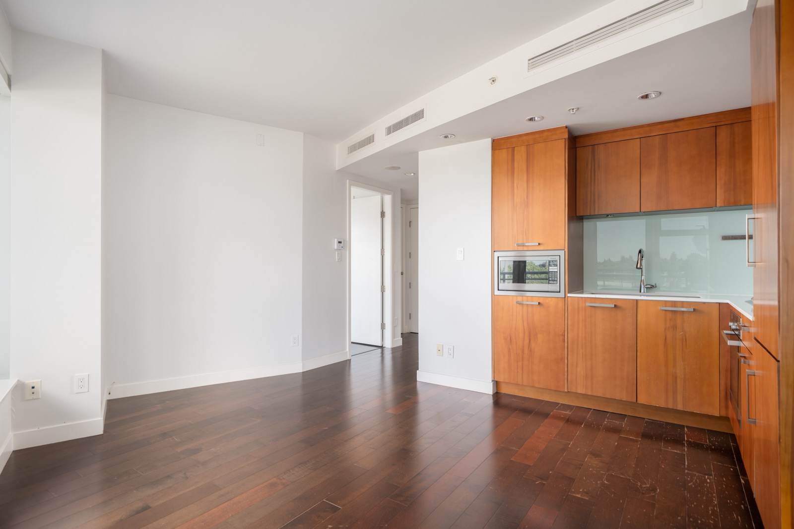Modern kitchen with wooden cabinets, glass backsplash, built-in microwave, and dark hardwood floors in a bright 6th-floor Vancouver apartment.