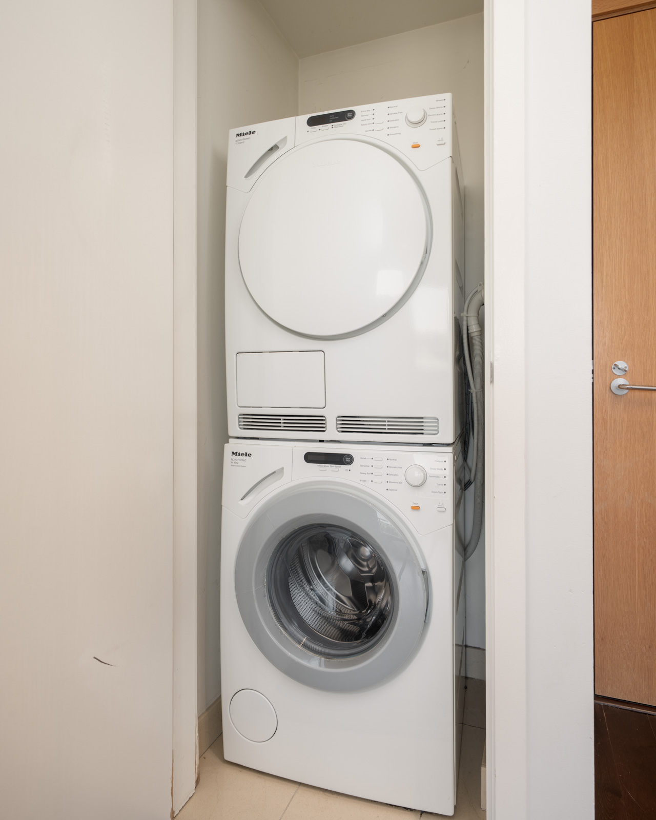 Stacked white washer and dryer in a small laundry nook at 1565 W 6th Ave, Vancouver, next to a closed wooden door.