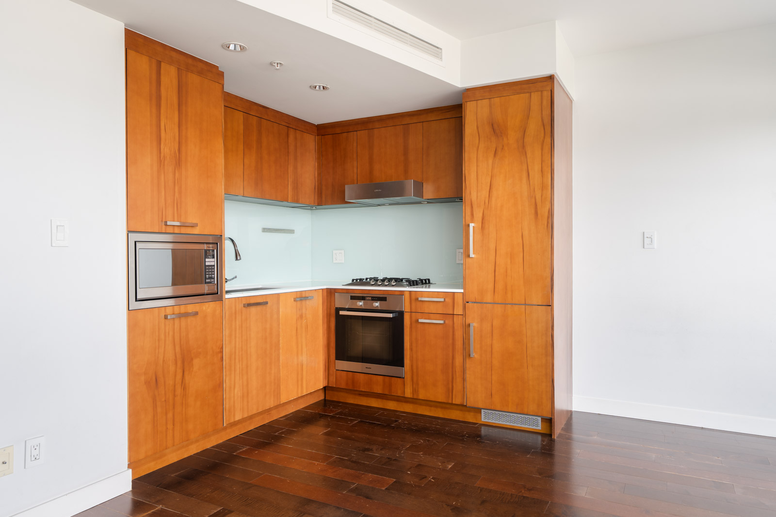 Modern kitchen on the 6th floor at 1565 W 6th Ave, Vancouver, with wood cabinets, stainless appliances, and glass backsplash.