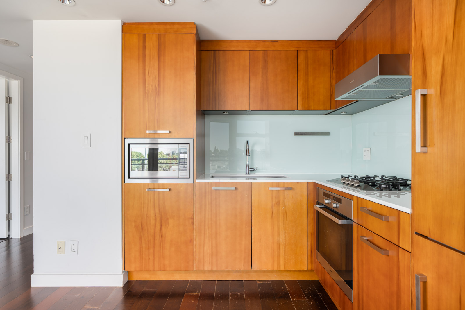 Modern kitchen with wood cabinets, built-in appliances, glass backsplash, and gas cooktop on dark floor in Vancouver.