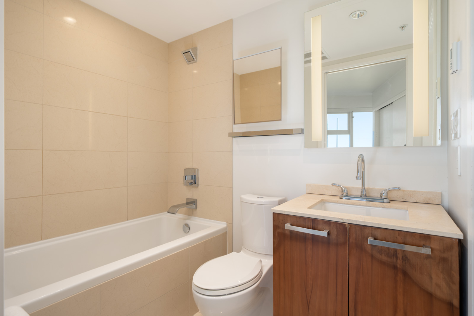 Modern bathroom on the 6th floor at 1565 W 6th Ave, Vancouver with bathtub, toilet, wood vanity, beige tiles, and large mirror.