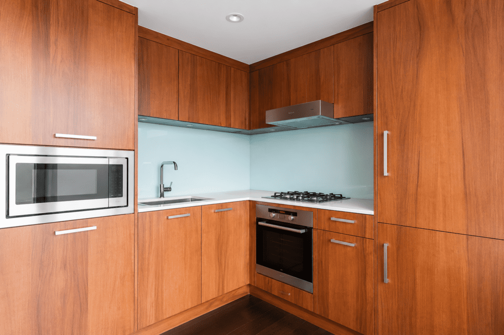 Modern kitchen with wooden cabinets, built-in microwave, oven, stovetop, sink, and a glass backsplash in the corner layout.