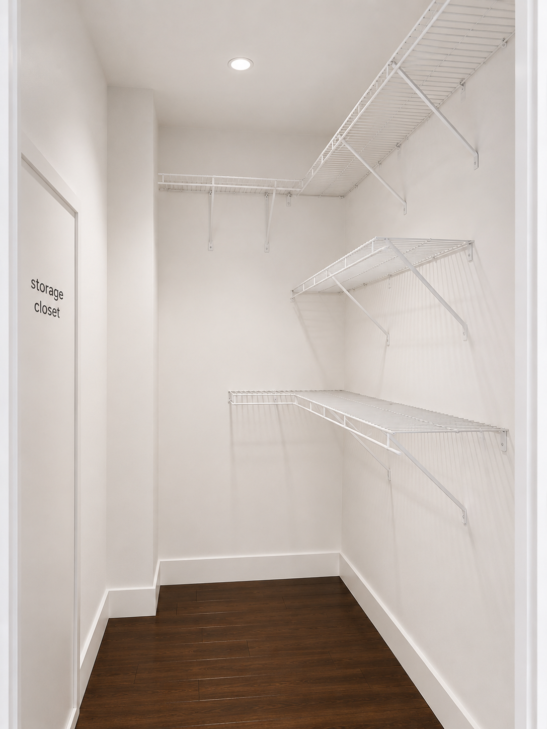 Empty storage closet with white walls, wire shelving on two sides, a ceiling light, and a door labeled 