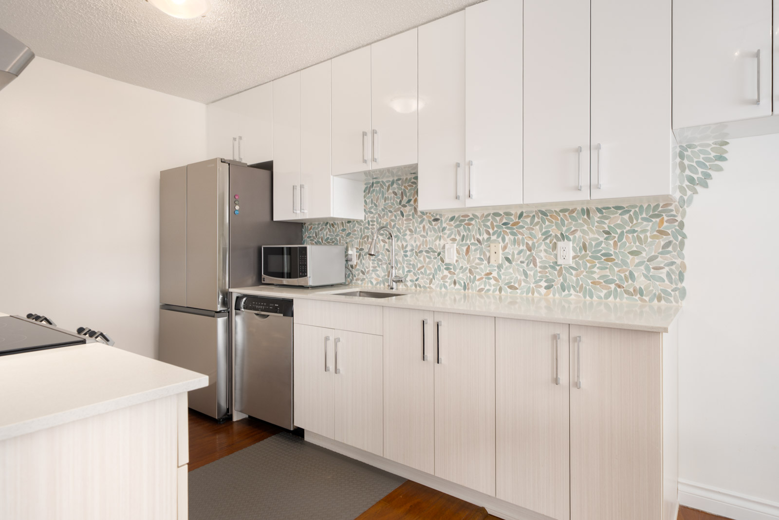 Modern kitchen featuring white cabinets, stainless steel appliances, leafy green and gray tile backsplash, and light wood floors.