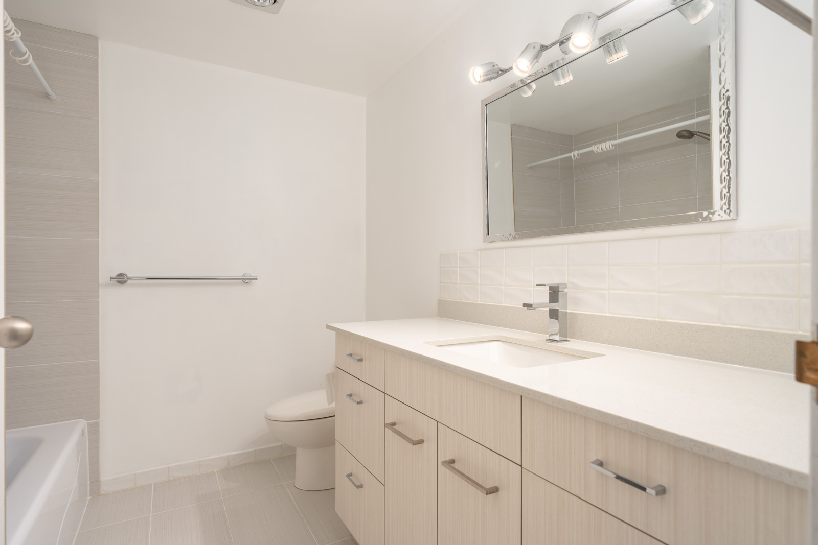Modern bathroom featuring a light wood vanity, rectangular sink, lit wall mirror, toilet, and bathtub with shower curtain.