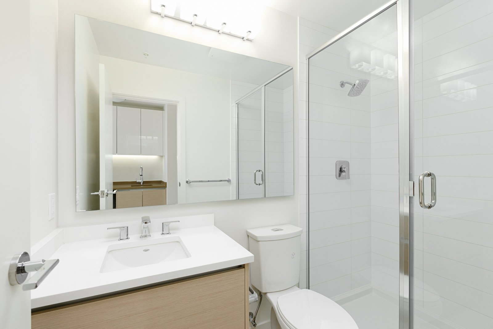 Modern bathroom with white walls, glass shower, toilet, large mirror, light fixture, and vanity at 8850 University Cres in Burnaby.