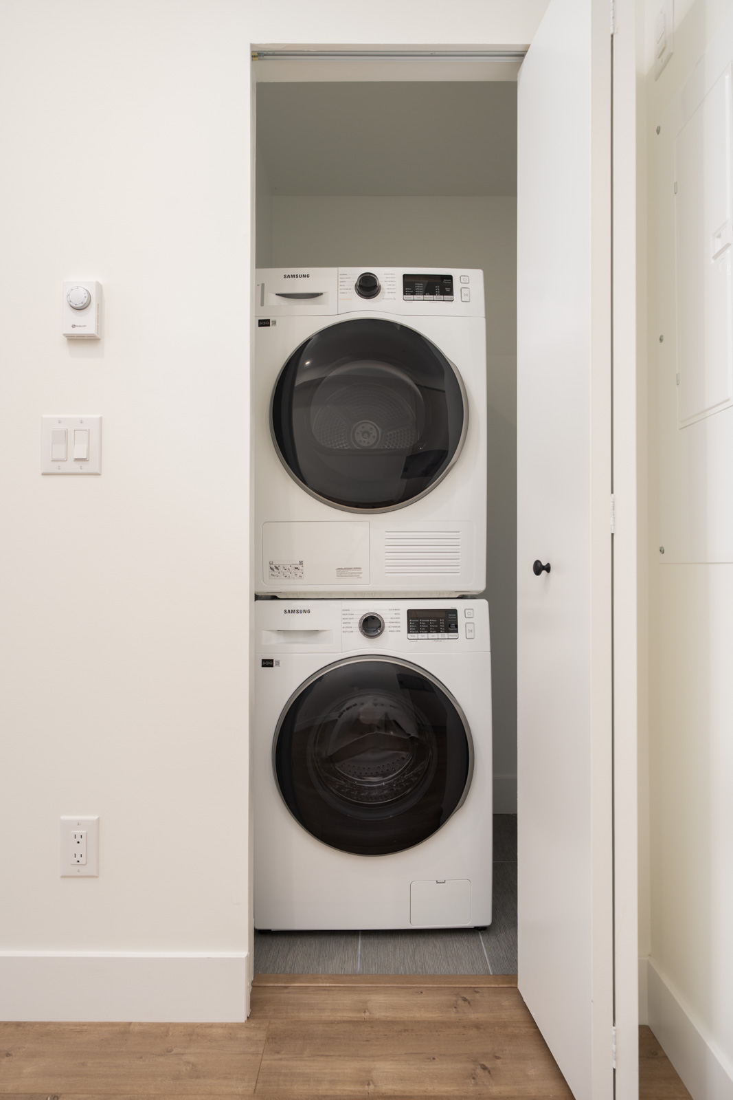 A stacked washer and dryer set is placed in a small laundry closet with the door partially open.