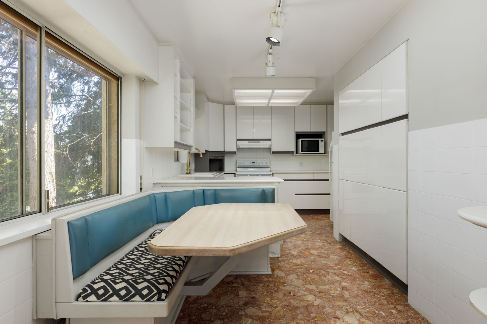 White kitchen at 6791 Griffiths Ave, Burnaby, with built-in appliances, marble floor, and corner dining nook by a large window.