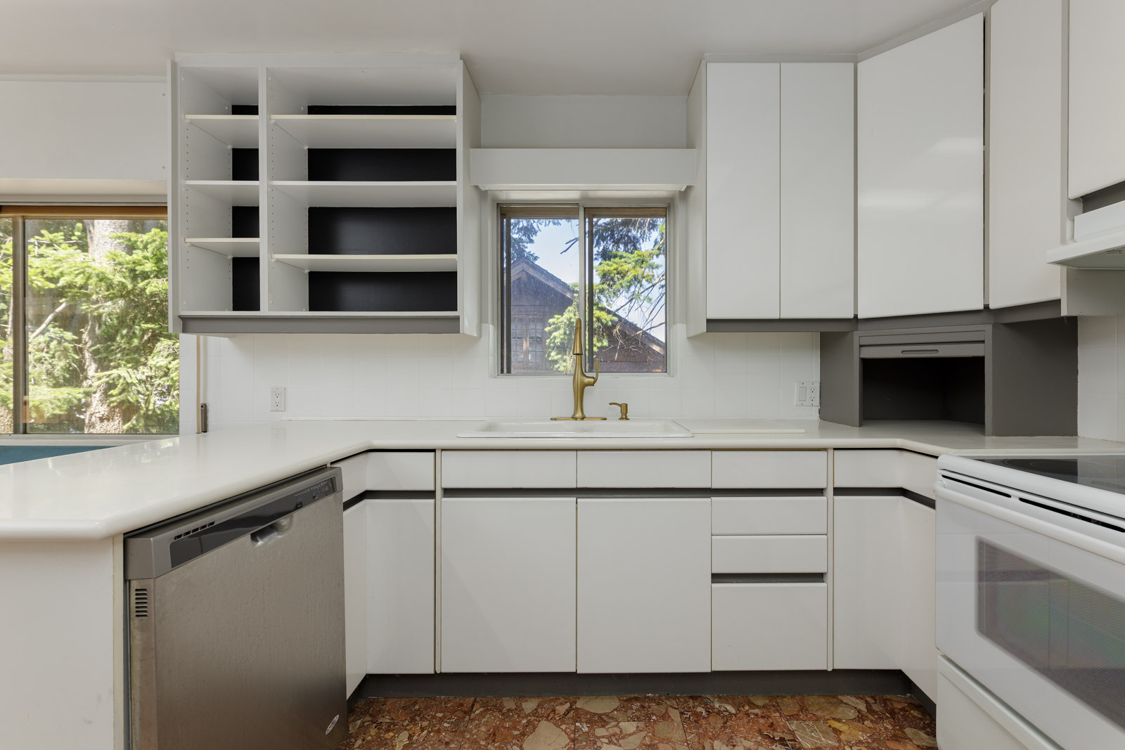 Modern kitchen in Upper Burnaby on Griffiths Ave with white cabinets, open shelves, stainless dishwasher, and brown patterned floor.