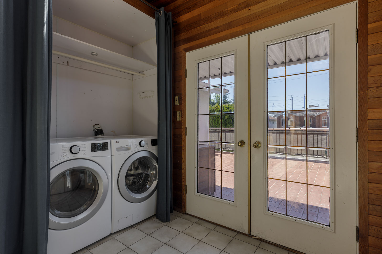 Laundry area with front-loading washer and dryer next to double glass doors to a patio in the upper suite on Griffiths Ave, Burnaby.