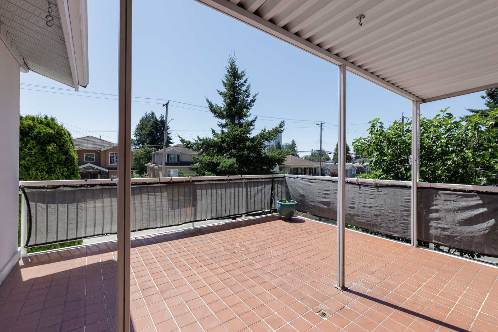 Covered patio with tiled floor, railing, and potted plant. Houses, trees, and power lines in background on Griffiths Ave, Burnaby.