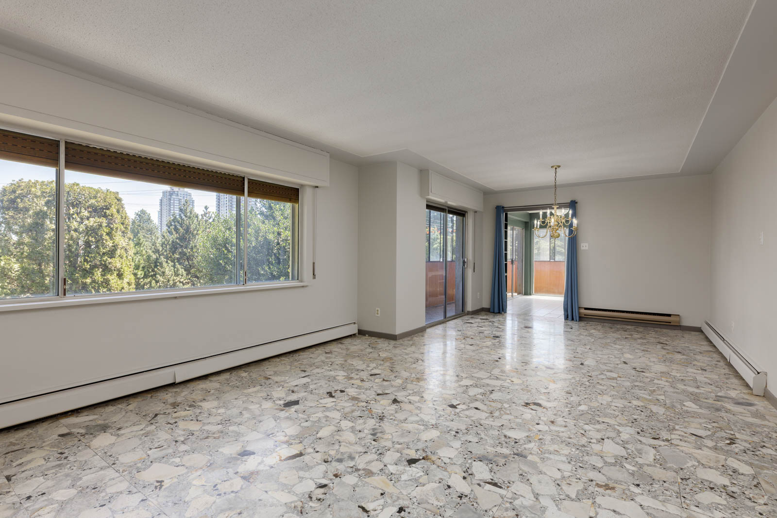 Unfurnished living and dining space in Upper Burnaby, with terrazzo floors, large windows, balcony access, and neutral walls.