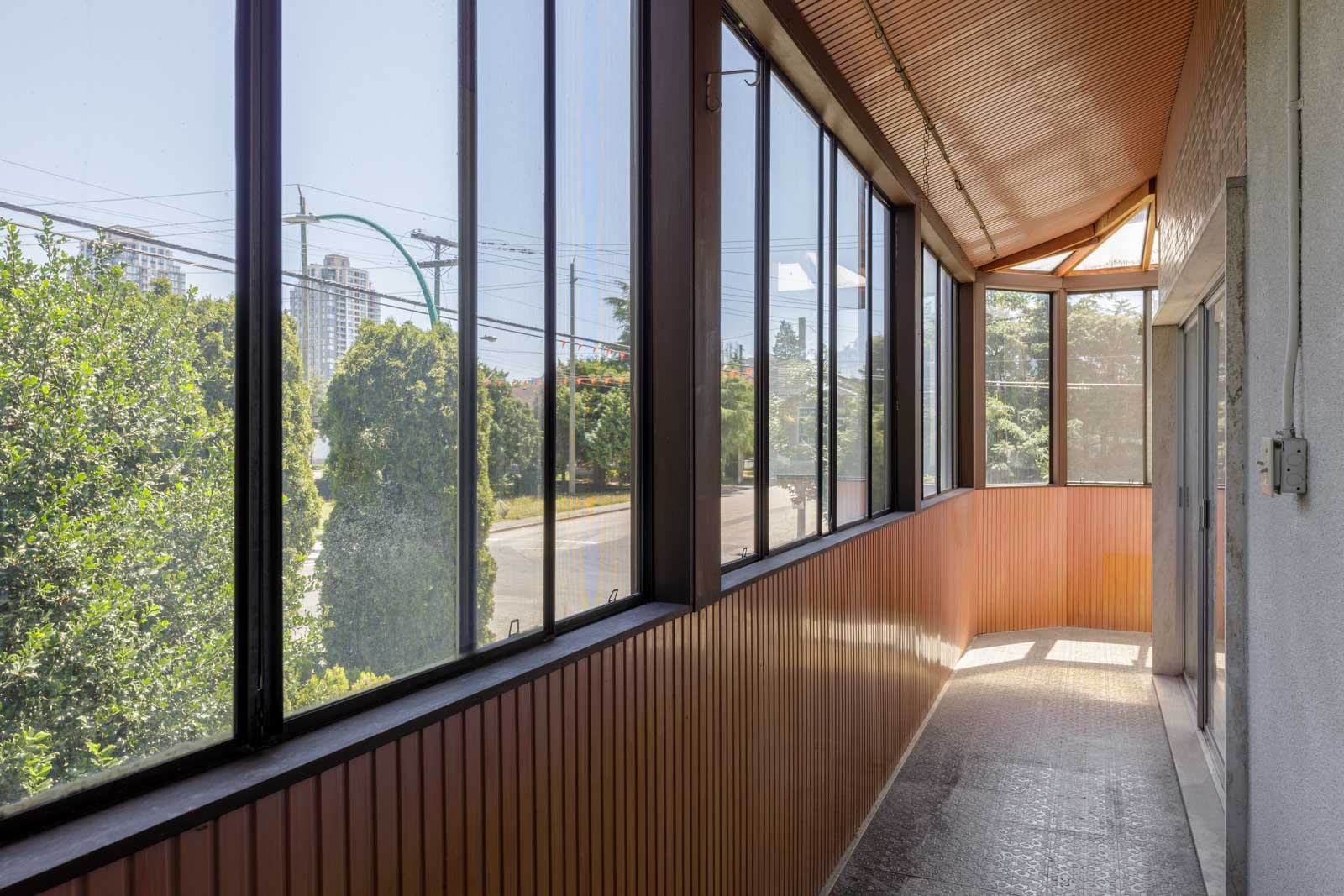 Enclosed balcony at 6791 Griffiths Ave, Burnaby, features large windows, brown paneling, tiled floor, city and tree views.