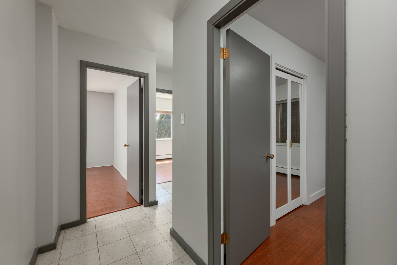 Hallway at 6791 Griffiths Ave, Burnaby, with gray doors to wood-floored rooms and one white-tiled room; one door has a glass panel.
