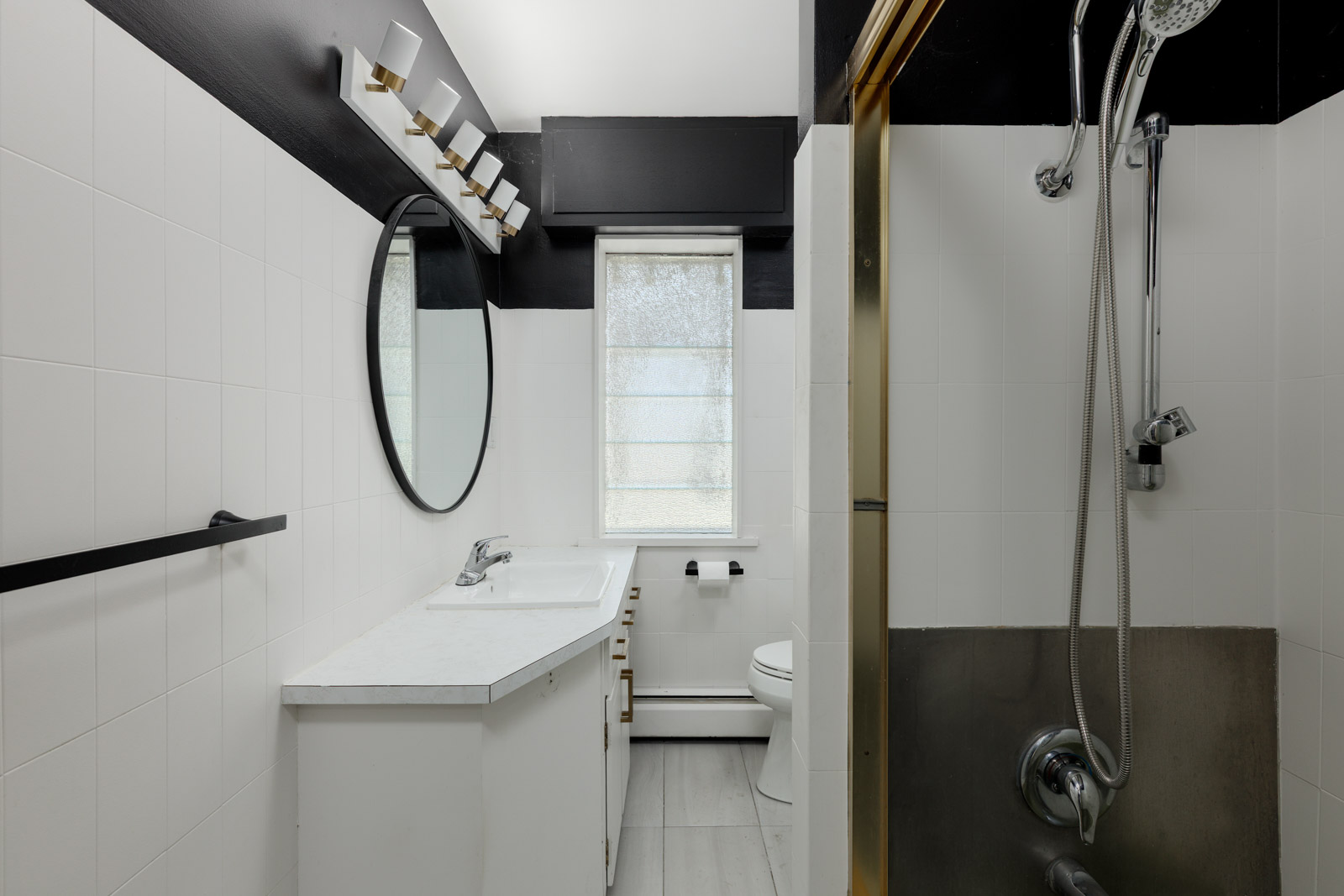 Modern bathroom on Griffiths Ave, Burnaby with round mirror, white counter, wall lights, window blind, and black-and-white decor.
