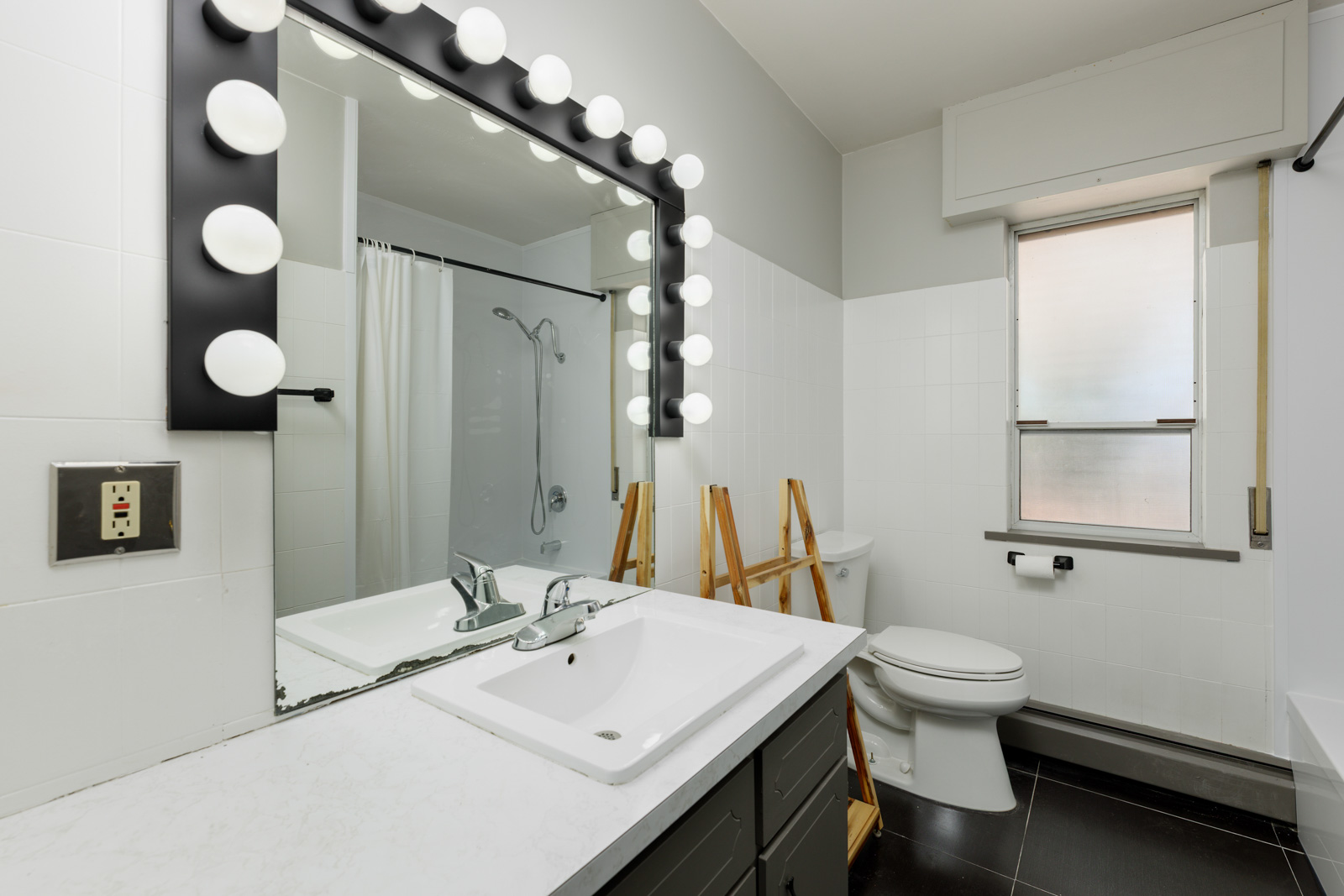 Modern bathroom at 6791 Griffiths Ave with a large mirror, round lights, white sink, toilet, frosted window, and shower curtain.