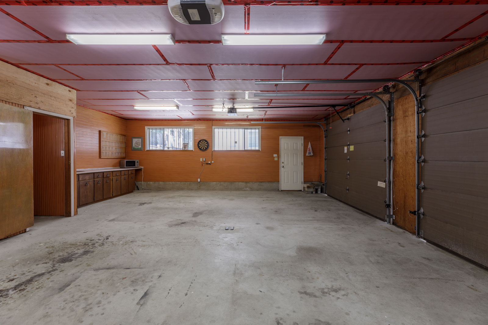 Two-car garage on Griffiths Ave, Burnaby; concrete floor, wooden cabinets, dartboard, fluorescent lights, insulated ceiling.