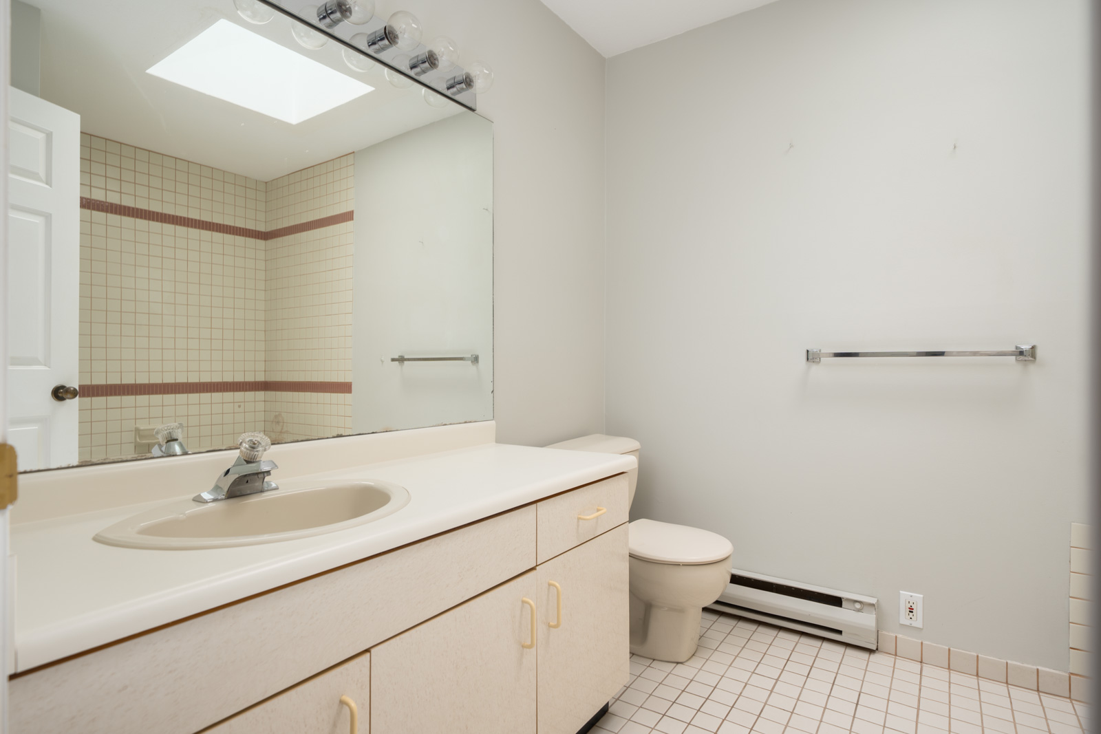 Bathroom with beige vanity, built-in sink, large mirror, toilet, towel rack, beige tiled floor, and shower visible in the mirror.