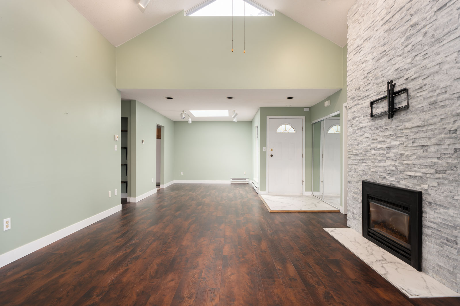 Living room with light green walls, dark wood floors, white stone fireplace, high ceiling, and a front door with sidelights.