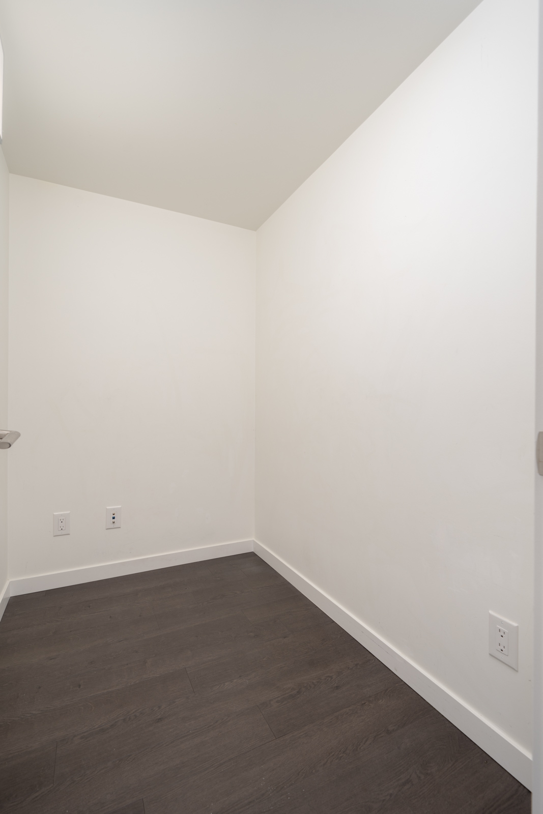 Empty room on 9th floor with white walls, dark wood floors, three outlets along the walls, Boundary Rd, Vancouver.