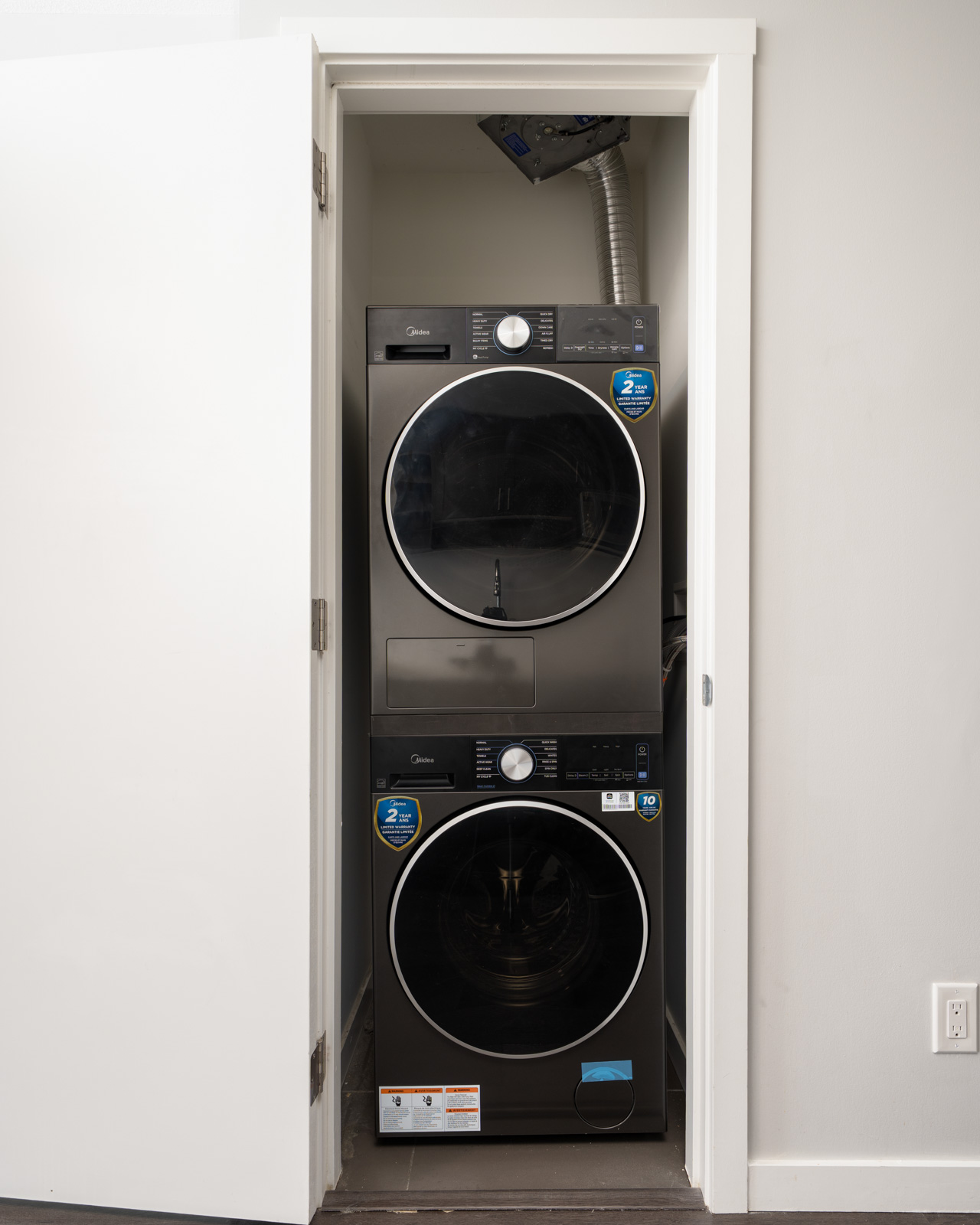 A stacked black washer and dryer sit in a small closet with a white door and gray walls on the 9th floor near Boundary Rd, Vancouver.